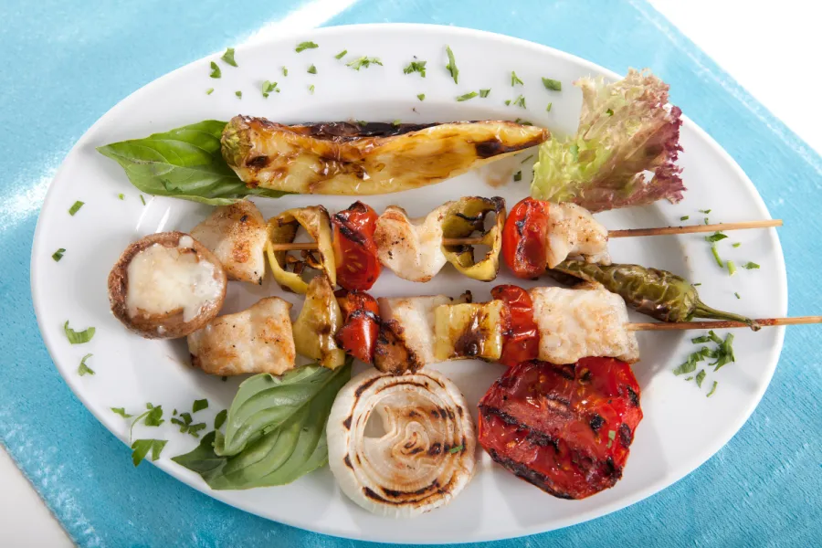 Pinchos de pescado acompañados de lechuga y hortalizas a la plancha.
