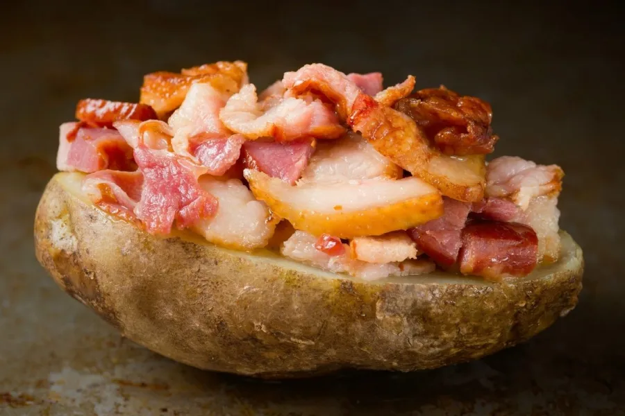 Media patata asada cubierta de beicon frito.