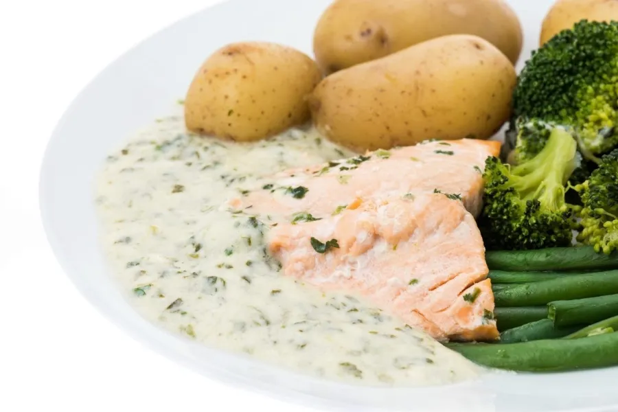 Un plato con salmón escalfado con salsa de berros y una guarnición de patatas y verduras cocidas.