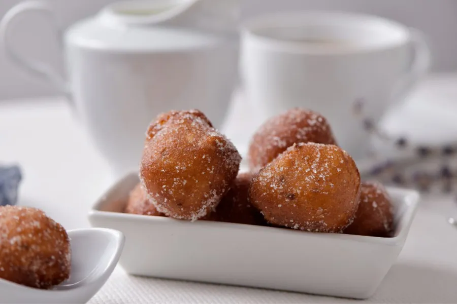 Buñuelos de Cuaresma en una fuente con un servicio de café al fondo.