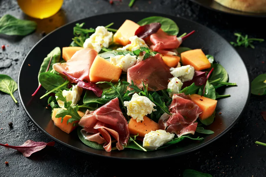Un plato con ensalada de melón con jamón de Parma y queso mozzarella.
