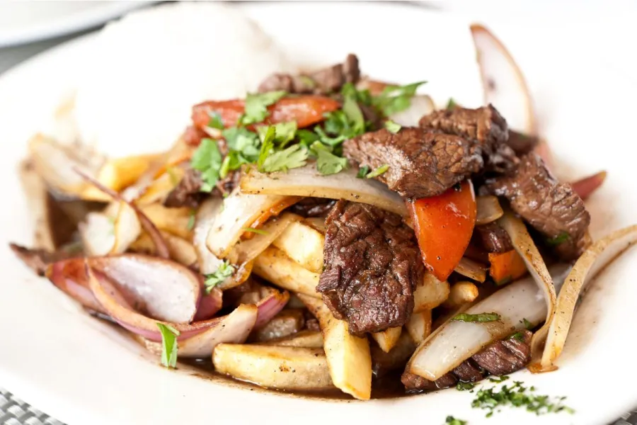 Un plato con lomo saltado, carne y verduras salteadas con paatas fritas y una salsa sabrosa.