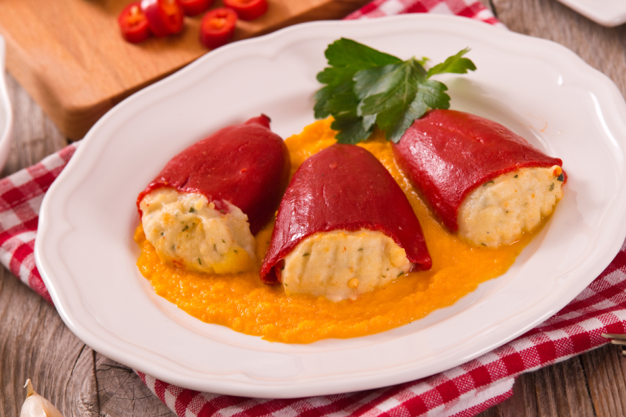 Un plato con tres pimientos de piquillo con un relleno de pescado con su salsa.