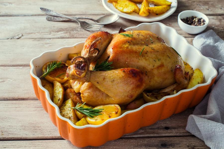 Pollo asado con limón y patatas en una fuente de horno de cerámica.