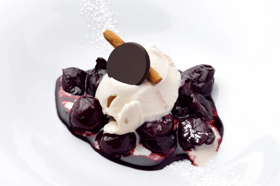 Cerezas al vino tinto acompañadas de helado, chocolate y canela en rama.