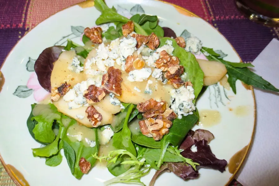 Un plato con ensalada de hojas variadas, queso azul, nueces y pera.