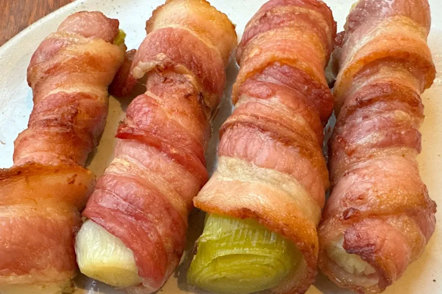 Puerros cocidos y después horneados con panceta ahumada.