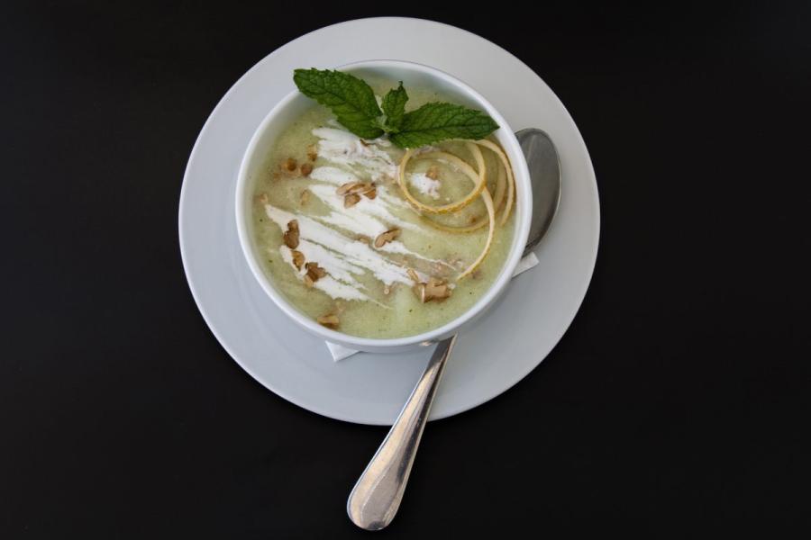 Un cuenco con gazpacho de melón decorado con menta, nata líquida y nueces.
