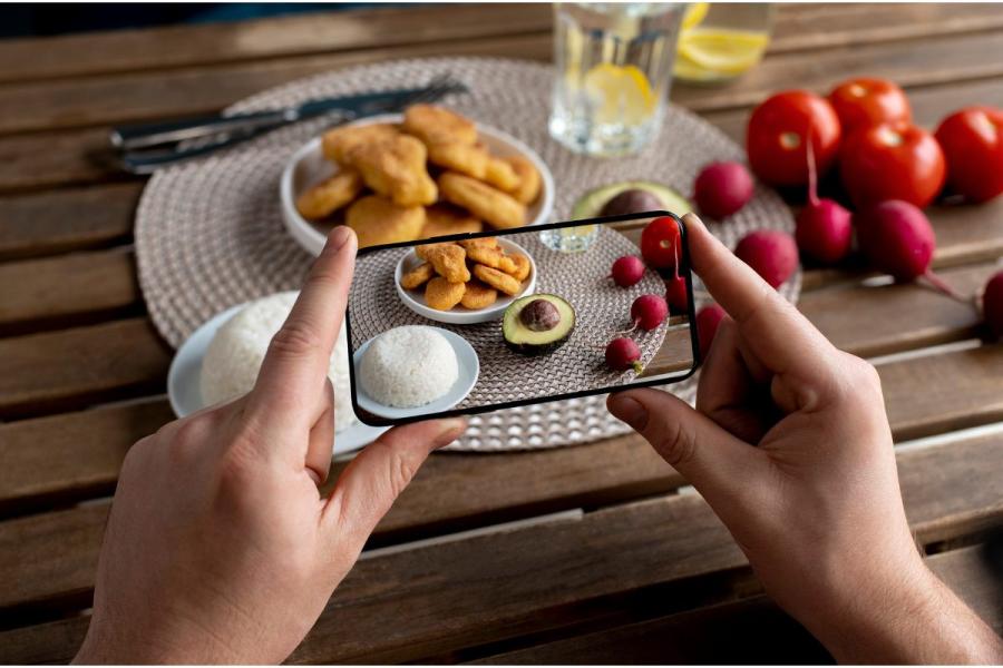 Un entusiasta de la gastronomía sacando una fotografía de la comida colocada en una mesa.