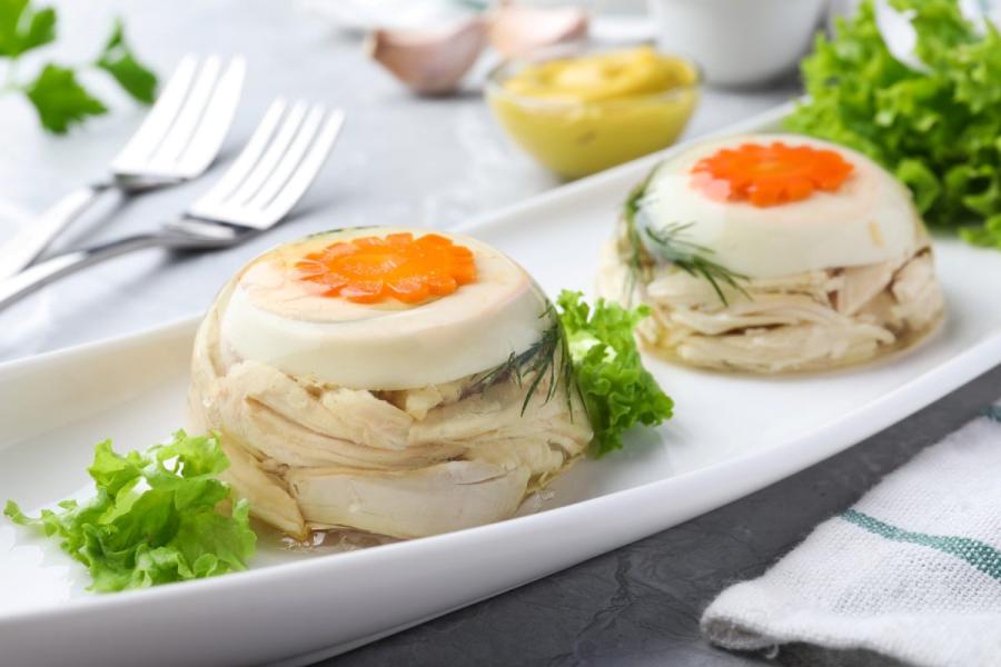 Dos áspic de ave de tamaño individual en una fuente blanca, adornados con hojas de ensalada.