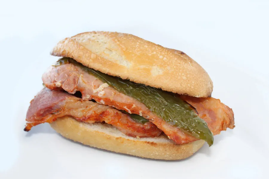 Un montadito de lomo en panecillo individual, con dos filetes de lomo de cerdo fritos y una tira de pimiento verde.