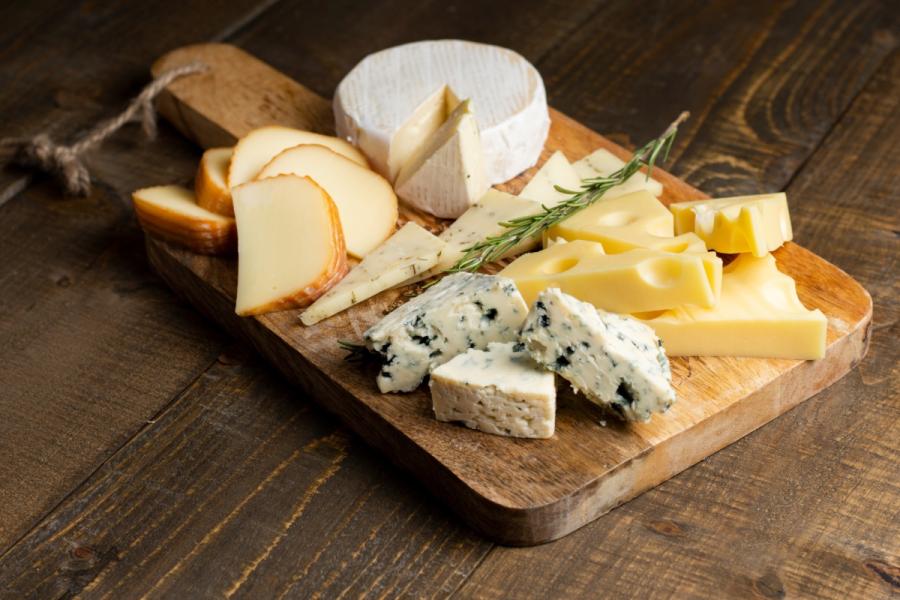 Tabla de quesos variados sobre una tabla de madera rústica, con queso de corteza blanca, queso azul, cuñas de queso semicurado, queso con agujeros tipo suizo y una ramita de romero.