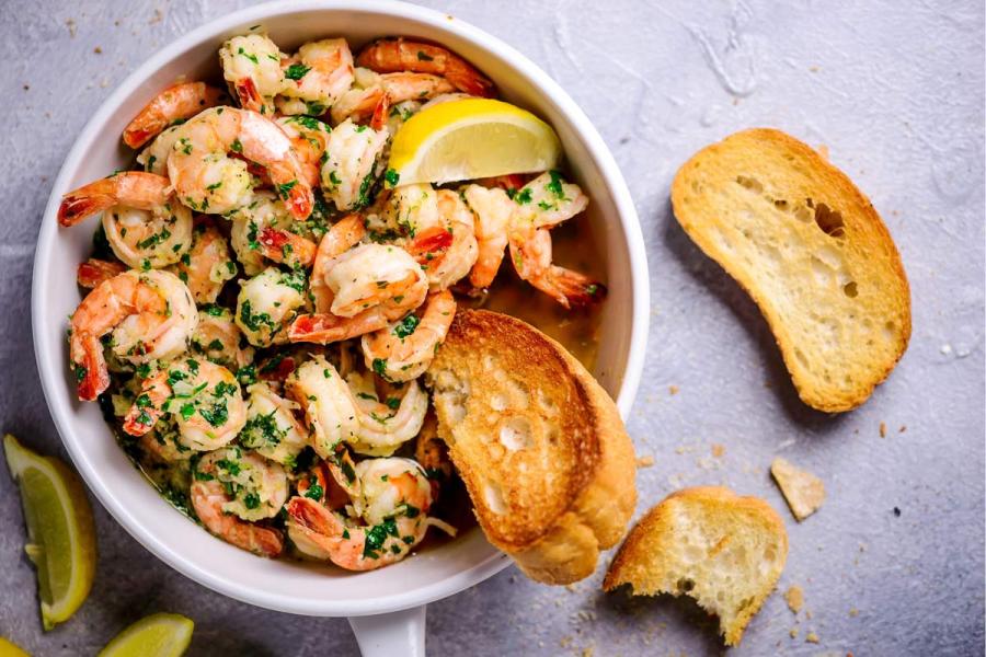 Gambas con salsa de mantequilla, ajo y limón en cacito de loza, acompañadas con rebanadas de pan tostado.