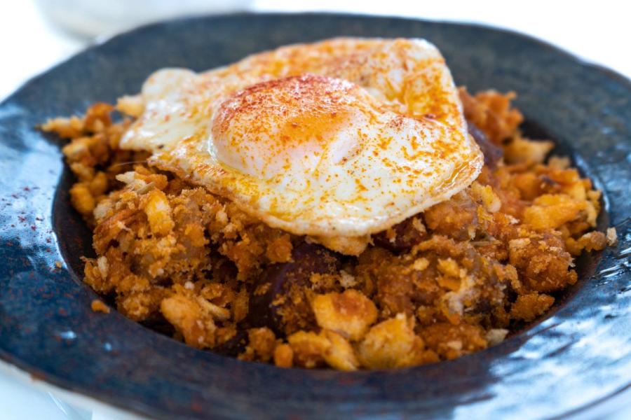 Huevo frito con migas decorado con pimentón en un plato oscuro.