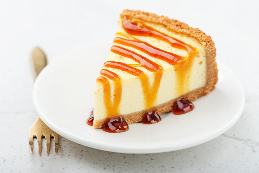 Porción de tarta de queso con salsa de caramelo sobre un plato blanco, acompañada de un tenedor dorado.