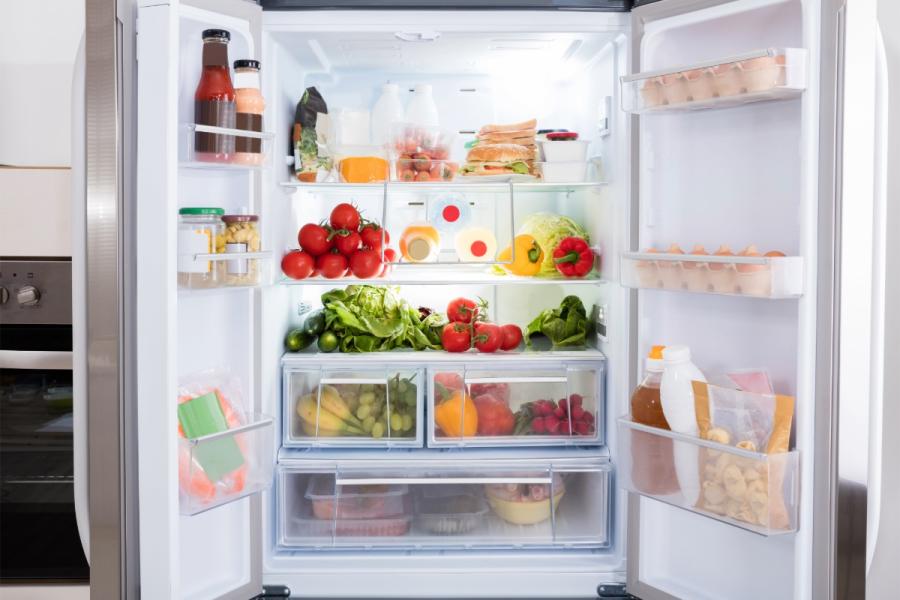 Frigorífico abierto con frutas, verduras, huevos, leche y otros alimentos frescos organizados en estantes y cajones.