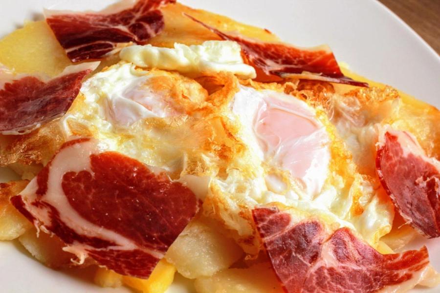 Detalle de unos huevos rotos con jamón serrano.