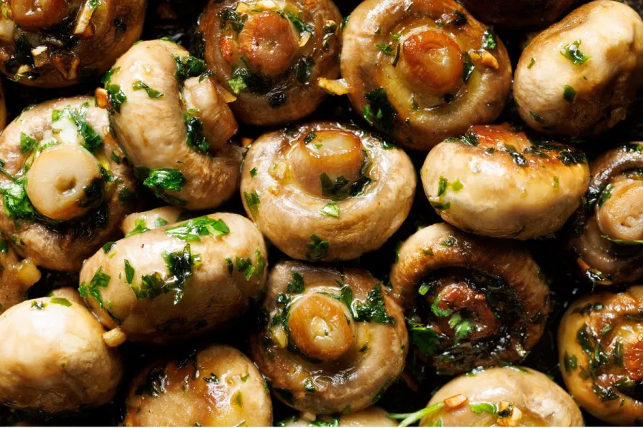 Champiñones enteros asados al horno, brillantes, con ajo picado y perejil fresco.