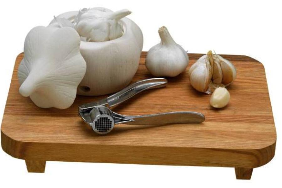Cabezas de ajo, dientes de ajo y prensa para ajos sobre una tabla de madera.