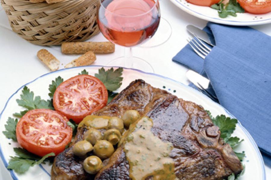 Chuletones de buey con sus guarniciones acompañados de vino tinto.