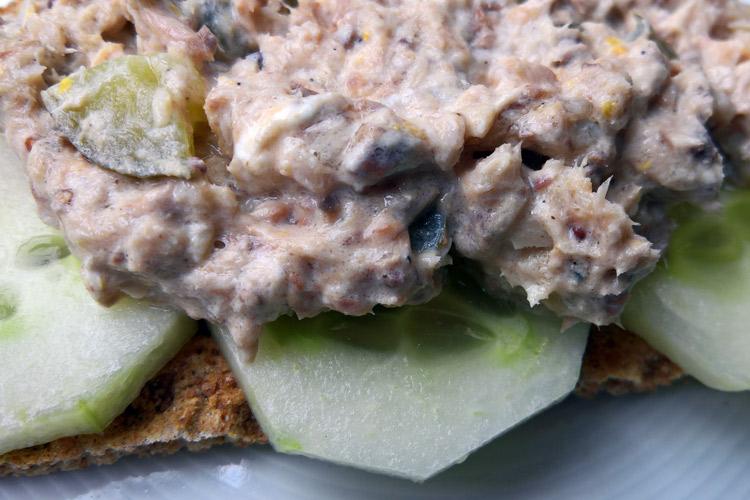 Primer plano de pasta de sardinas sobre rodajas de pepino en una galleta salada.