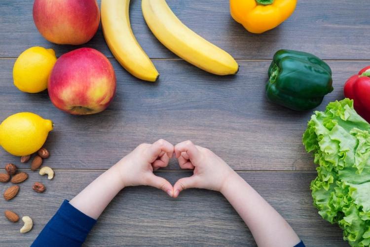 Frutas, verduras y nueces y las manos de un niño formando un corazón.