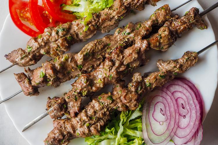 Kebabs de cordero en brochetas de metal acompañados de ensalada.