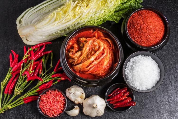 Un recipiente con kimchi casero rodeado de los ingredientes necesarios para prepararlo.