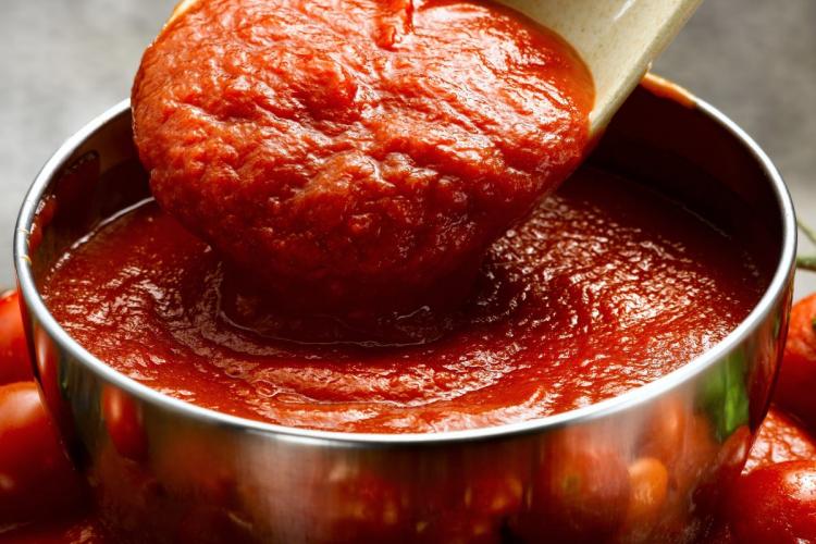 Una cuchara deja caer salsa de tomate en un recipiente lleno de la misma salsa, probablemetne para comprobar la textura.